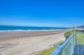 Expansive sandy beach stretches along pristine coastline with rolling waves and distant cliffs under clear blue skies.