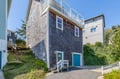 Charming shingled vacation home on a hillside with a rooftop deck, bright turquoise door, and nearby parking—your coastal retreat awaits.