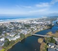 Aerial view of a charming coastal town nestled between wide sandy beaches and a serene river, with misty hills rolling in the distance.