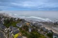 Aerial view of coastal homes nestled between lush greenery and pristine sandy beach with gentle waves rolling ashore.