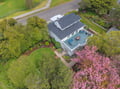 Aerial view of the property showcasing the main building with rooftop pool, surrounded by lush gardens and blooming cherry trees in a peaceful residential neighborhood.