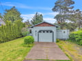 Charming coastal cottage nestled among towering pines and lush greenery, offering a peaceful retreat in a quiet neighborhood setting.