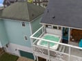 An aerial view shows the rooftop hot tub on the upper deck, offering a private retreat for relaxation. The property is located in a coastal residential neighborhood with nearby homes visible.