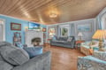 Sink into comfortable seating by your cozy fireplace, surrounded by coastal artwork and warm wood ceilings that create the perfect retreat atmosphere.