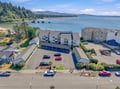 Aerial view of coastal property featuring multi-building vacation rental complex with bay and mountain backdrop in scenic Pacific Northwest setting.
