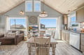 Sunlit open-concept space blends cozy dining and living areas with ocean views through expansive windows. Your coastal retreat features charming vaulted ceilings, rustic details, and a fully-equipped kitchen ready for your stay.