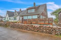 Charming coastal cottage with distinctive stone retaining wall and wooden deck, nestled in a picturesque seaside neighborhood.