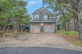 Charming shingled home nestled among mature trees in a quiet residential neighborhood, featuring a two-car garage and welcoming entrance.