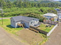 Aerial view of the property nestled in a quiet coastal neighborhood, surrounded by lush greenery and forested mountains.