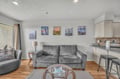 Sink into the plush gray sofa in your open living space, where modern comfort meets coastal charm through curated artwork and warm hardwood floors.