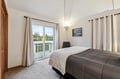Wake up in your peaceful bedroom with natural light streaming through balcony doors and cozy bedding for restful nights.