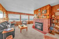 Cozy up by your crackling fireplace while watching waves through panoramic windows in this warm, wood-paneled oceanfront living room.
