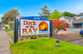 Dock of the Bay Condominiums sits in a welcoming coastal neighborhood, marked by colorful blooms and mature trees along a quiet residential street.