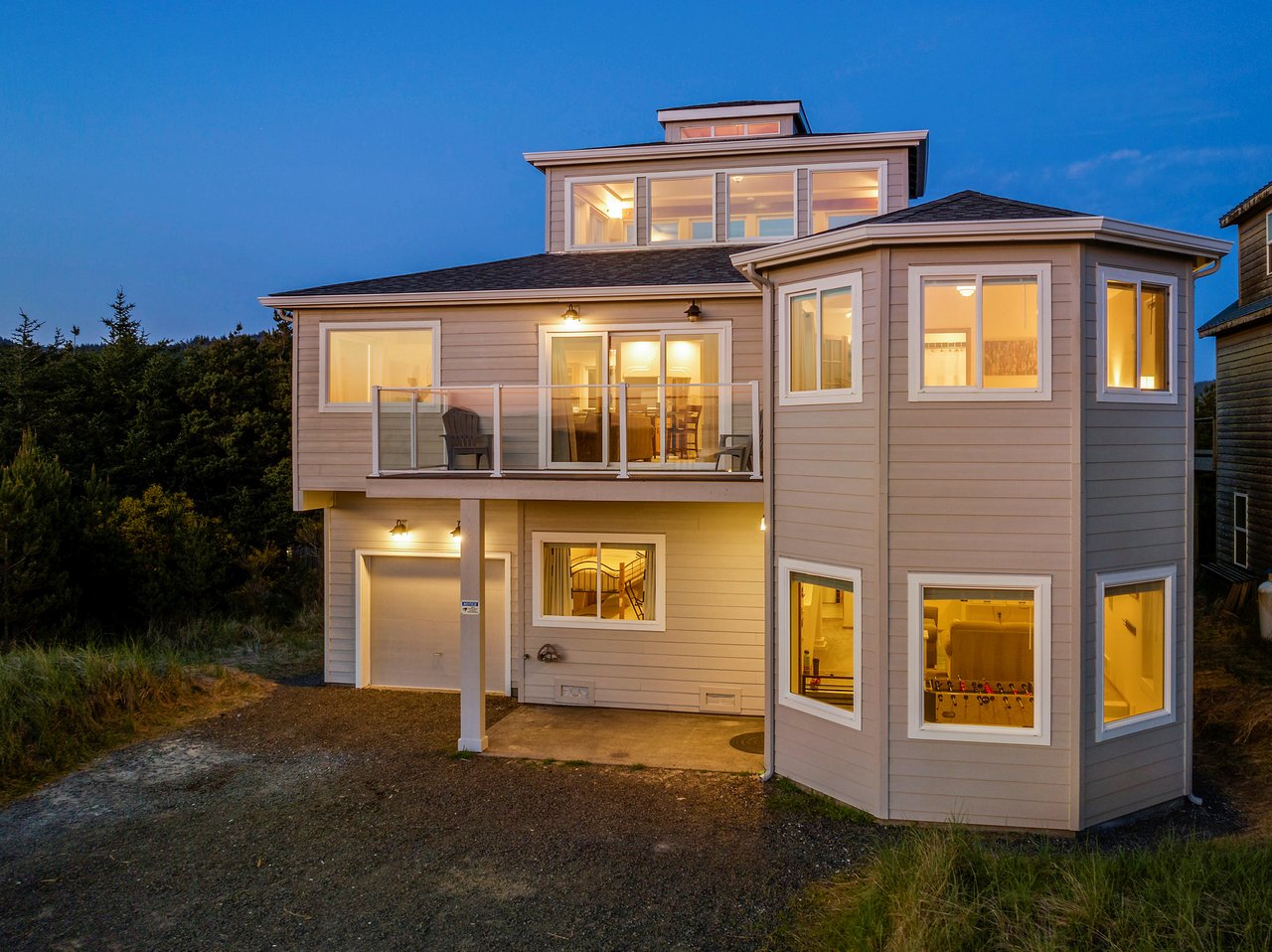 Modern coastal home with warm evening lighting and multi-level design surrounded by natural landscaping.