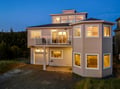Modern coastal home with warm evening lighting and multi-level design surrounded by natural landscaping.