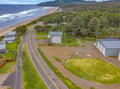 Aerial view of the property nestled between forested hillsides and a sandy beach, with direct access to the scenic coastal highway and ocean just steps away.