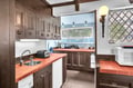 Prepare delicious meals in this spacious kitchen featuring terra-cotta tile countertops, rustic wood cabinets, and charming exposed beams overhead.
