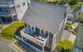 Aerial view of a charming coastal vacation rental featuring a spacious upper deck with dining and lounge seating, nestled in a quiet residential neighborhood near the beach.