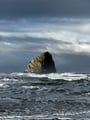 Dramatic coastal scenery with waves crashing against a prominent rock formation under cloudy skies.