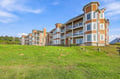 A coastal multi-unit property surrounded by lush green lawns, with distinctive architectural features and views of the natural landscape beyond.