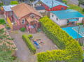 Aerial view of the property showing the main vacation rental building with its distinctive brown exterior, surrounded by neighboring homes in a quiet residential area with mature landscaping and nearby amenities.
