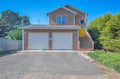 Charming coastal-style home with cedar shingles and bright yellow door, featuring convenient garage parking and lush green surroundings.