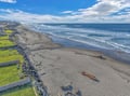 Expansive coastline with pristine sandy beach stretching along the Pacific Ocean, featuring dramatic waves and coastal terrain.