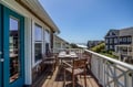 A private deck offers coastal living at its best, with inviting seating and glimpses of the ocean beyond neighboring beach homes under a clear blue sky.