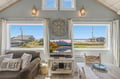 Curl up in this coastal living room where ocean breezes meet mountain views. Natural light pours through multiple windows, highlighting cozy seating and beachy decor that invite your seaside escape.