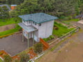 Modern two-story vacation home surrounded by lush evergreen forest with spacious yard, landscaped grounds, and ample parking near the entrance.