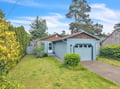 A charming coastal cottage nestled in a peaceful neighborhood, surrounded by mature trees and lush greenery, with convenient parking and nearby beach access.