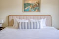 Sink into crisp white linens and plush pillows on this inviting bed, framed by a stylish upholstered headboard with coastal artwork above for your peaceful getaway.