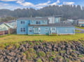 Charming blue coastal home nestled between forested hills and rocky shoreline in a peaceful neighborhood setting.