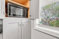Your kitchen is thoughtfully equipped with a built-in microwave tucked neatly above clean white cabinetry, making meal prep easy and convenient. Natural light streams in through the window, brightening the space as you cook.