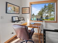 Your workspace features a sleek wooden desk by a large window, where natural light streams in as you work with treetop views.