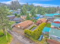 An aerial view captures the property nestled within a peaceful coastal neighborhood surrounded by lush evergreen trees and colorful homes.
