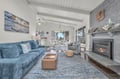 Unwind in your coastal-inspired living space with cozy fireplace, ocean artwork, and natural light streaming through windows.