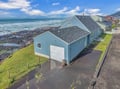 Charming blue oceanfront home positioned directly on the rugged coastline with dramatic waves crashing against rocky shores.