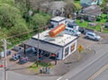 Aerial view of a quirky neighborhood restaurant featuring a giant hot dog sculpture on its roof, complete with outdoor seating.