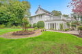 Charming white property with beautifully landscaped gardens, mature trees, and spacious grounds in a peaceful residential setting.