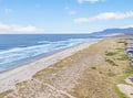 Aerial view of pristine coastline with sandy beach, rolling waves, and coastal properties nestled between ocean and mountains.
