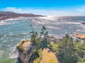 Stunning aerial view of dramatic coastal cliffs meeting pristine ocean waters, with rugged coastline stretching toward distant mountains.