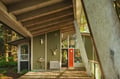 A modern cabin entrance with covered deck showcasing unique architecture surrounded by lush forest setting.