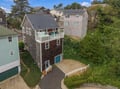 Aerial view of a charming coastal property featuring a spacious multi-level design with private balcony and deck areas, nestled among lush trees in a peaceful neighborhood.