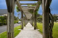 A charming wooden pergola walkway leads through the peaceful neighborhood, creating a scenic pathway surrounded by lush gardens and local homes.