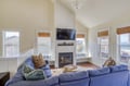 Unwind in your bright living room, where vaulted ceilings and a cozy fireplace create the perfect retreat. Sunlight streams through multiple windows as you sink into plush seating, ocean views just beyond.
