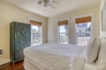 Relax in this light-filled bedroom where crisp white linens and natural bamboo shades create a serene coastal retreat. Large windows frame views of the surrounding neighborhood.