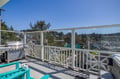 Elevated deck overlooks a peaceful residential neighborhood backed by evergreen forests. Modern glass railing and BBQ grill await outdoor gatherings.