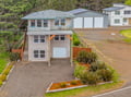 Aerial view of a multi-story vacation rental home with modern design, surrounded by lush greenery and neighboring properties in a peaceful residential setting.