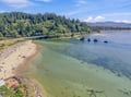 An aerial view captures the stunning coastal area surrounding the property, featuring a pristine sandy beach, tranquil turquoise waters, and forested hills under bright summer skies.